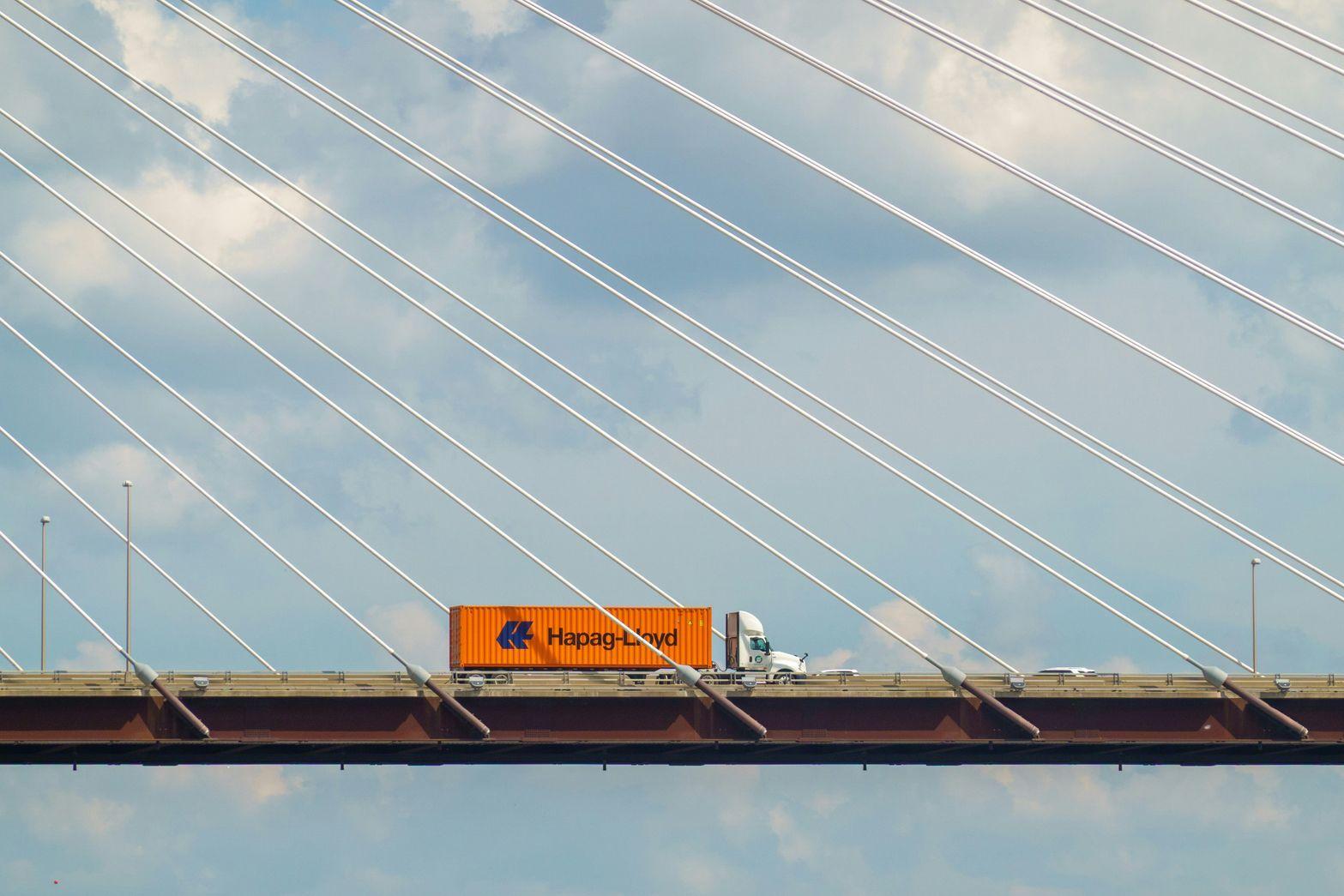 Semi truck hauling Hapag-Lloyd container crossing cable-stayed bridge