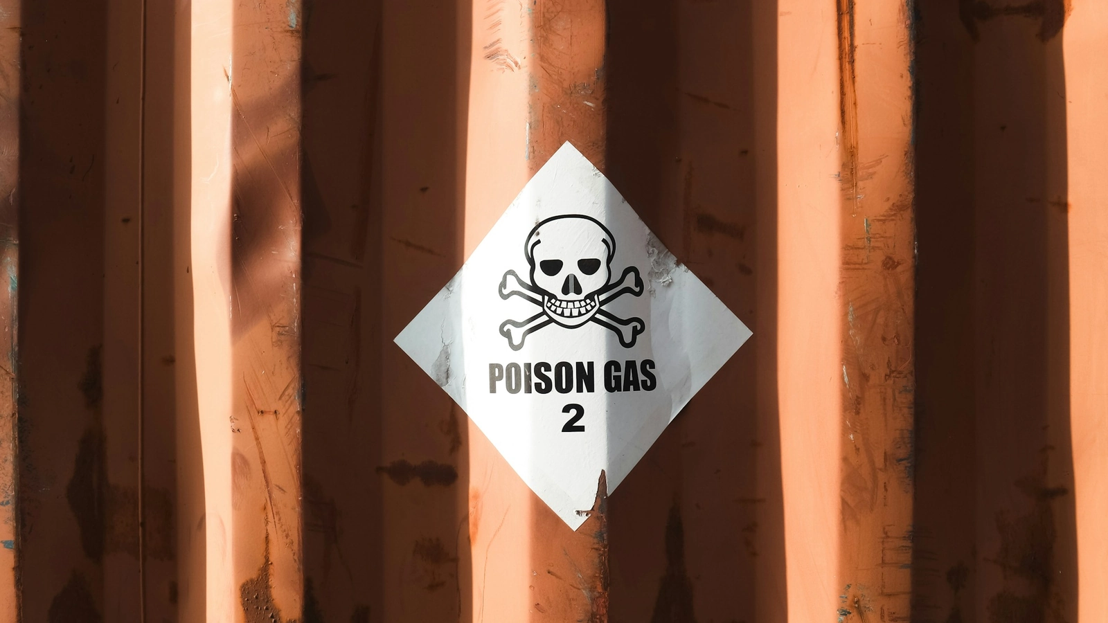 A Class 2.3 "POISON GAS" dangerous-goods placard with a skull-and-crossbones symbol affixed to the corrugated steel side of an orange ocean shipping container.
